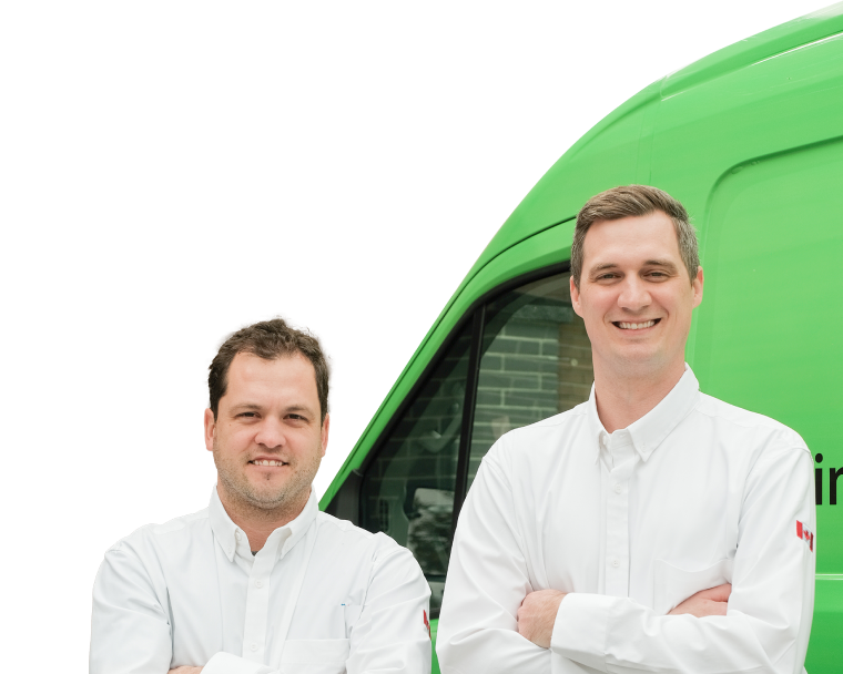 Two Limcan Certified technicians smiling in front of their green service van, wearing issued jackets during an on-site consultation.