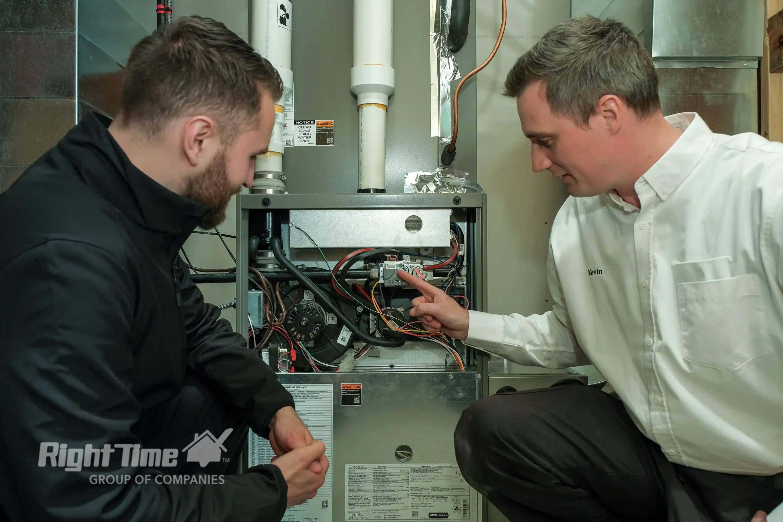 Two HVAC technicians are inspecting an open gas furnace and pointing to components during an airflow/diagnostic check.